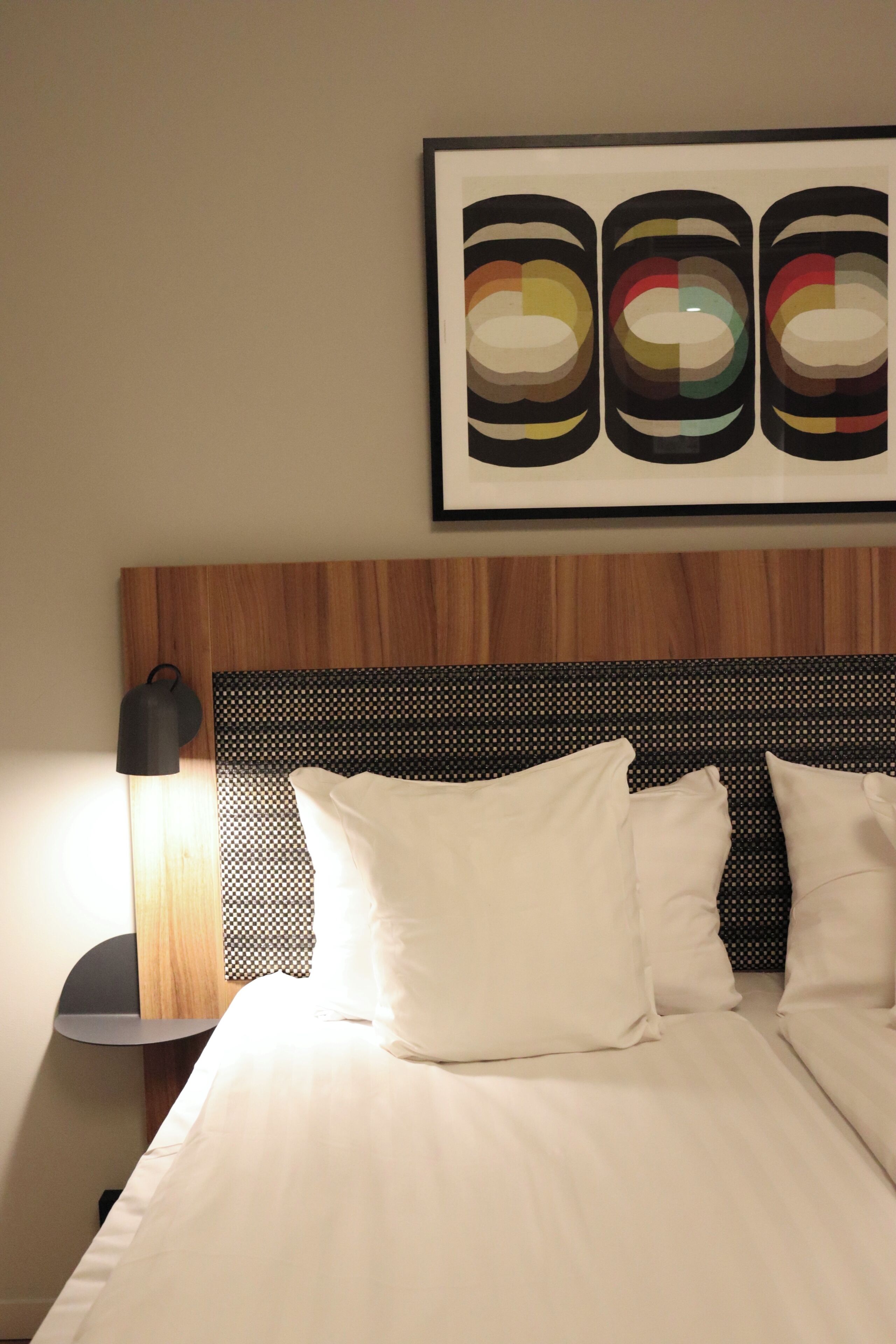A neatly made bed with white linens, a wooden headboard, and a black and white patterned pillow.