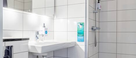 A modern bathroom with a white sink, a mirror, a shower with a handheld showerhead, and black tiled flooring.