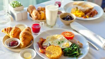 Una mesa de desayuno con cruasanes, huevos, tocino, tostadas y diferentes mermeladas.