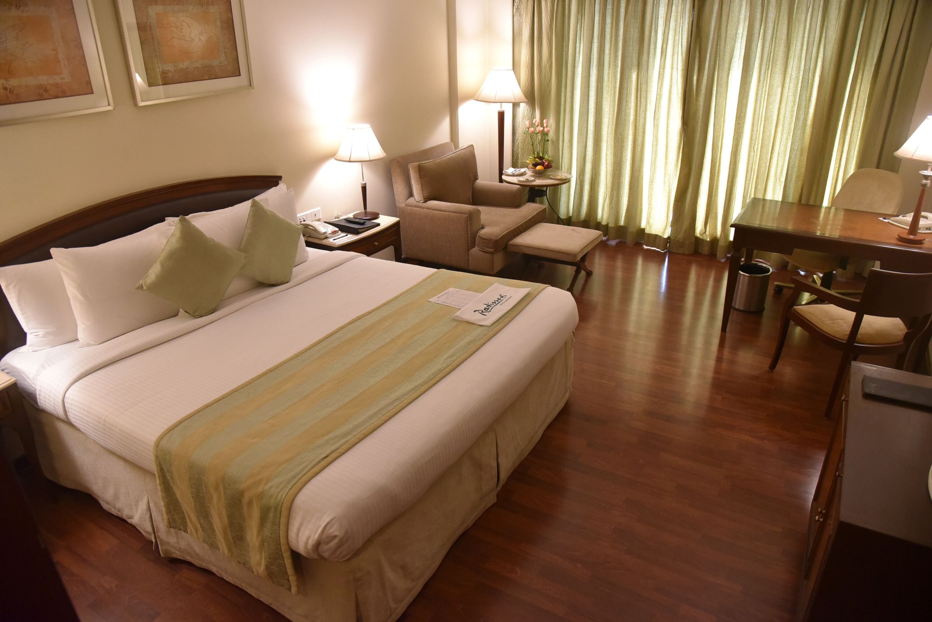 Une chambre d’hôtel avec un grand lit, deux tables de chevet, un bureau, une chaise et un rideau.