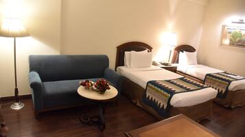 Habitación de hotel con dos camas, un sofá, una mesita con un jarrón de flores y una lámpara.