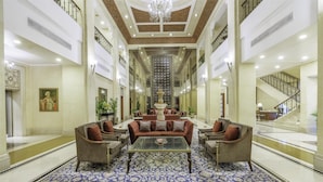 A spacious lobby with a central seating area, a grand staircase, and a chandelier. - Radisson Hotel Varanasi (Varanasi)