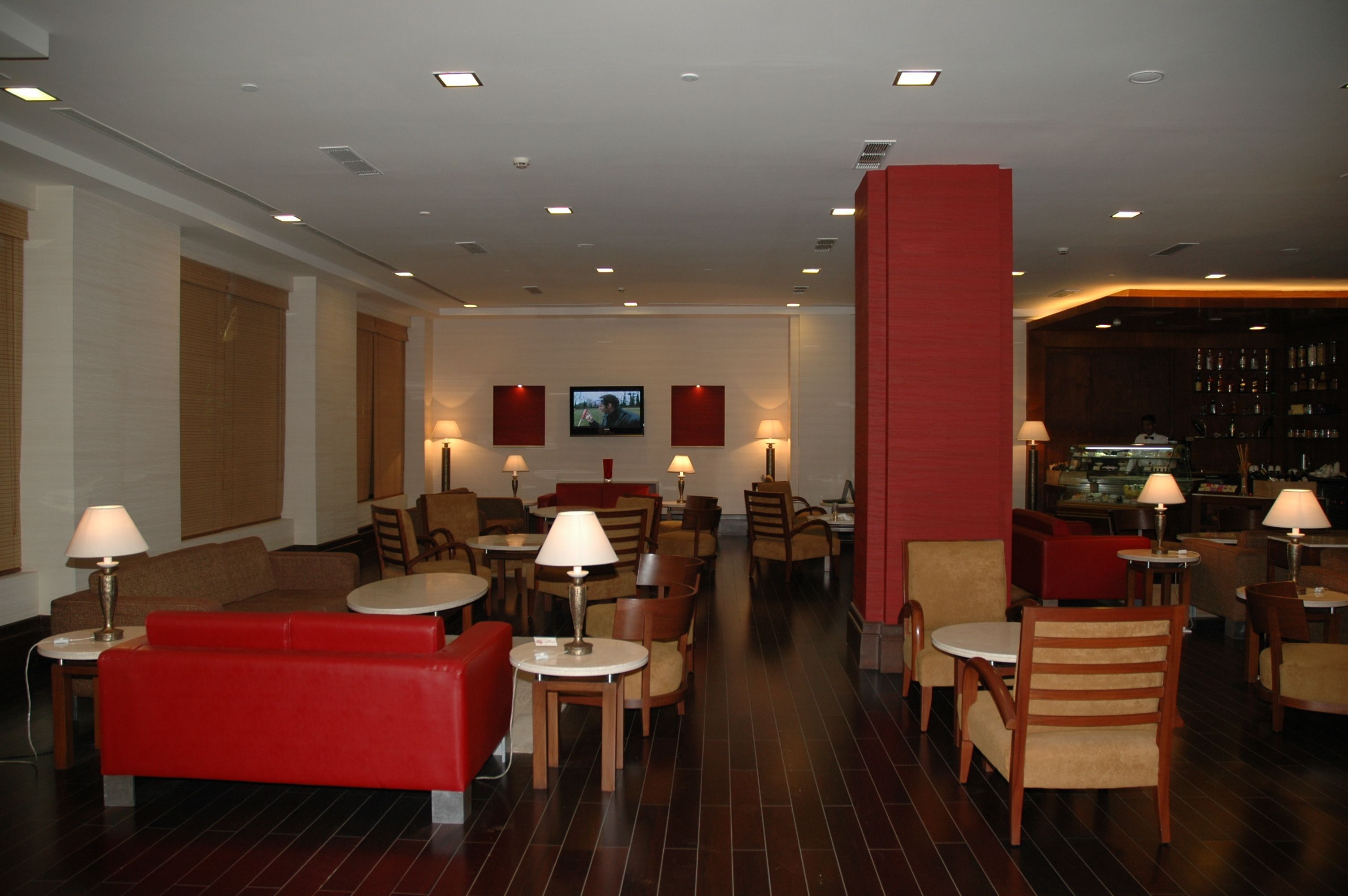 A hotel lobby with red sofas, wooden chairs, tables, and a bar area.