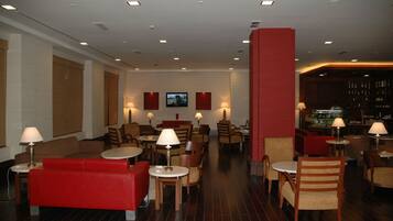 A hotel lobby with red sofas, wooden chairs, tables, and a bar area.
