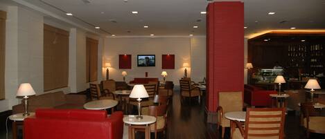 A hotel lobby with red sofas, wooden chairs, tables, and a bar area.