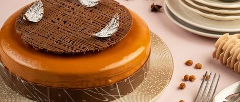 Un pastel redondo con una cubierta de celosía de chocolate y hojas plateadas decorativas, sobre un pedestal dorado.