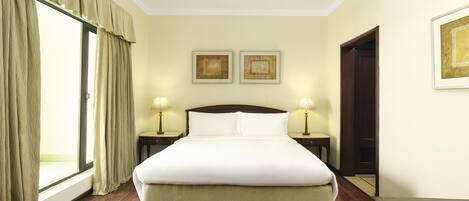 A hotel room with a large bed, two bedside lamps, a window with curtains, and two framed pictures on the wall.