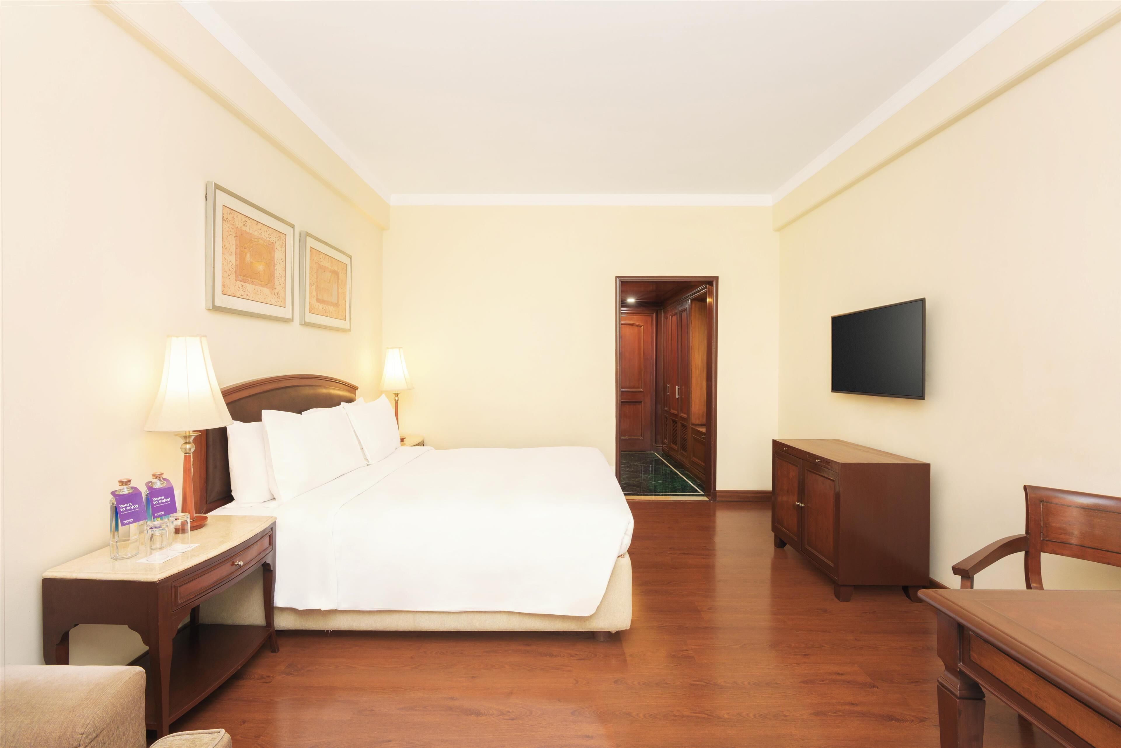 A hotel room with a bed, bedside tables, a TV, and a wooden wardrobe.