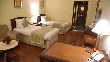 A hotel room with two beds, a desk, a chair, a small table with a vase of flowers, and a sign indicating guest satisfaction.