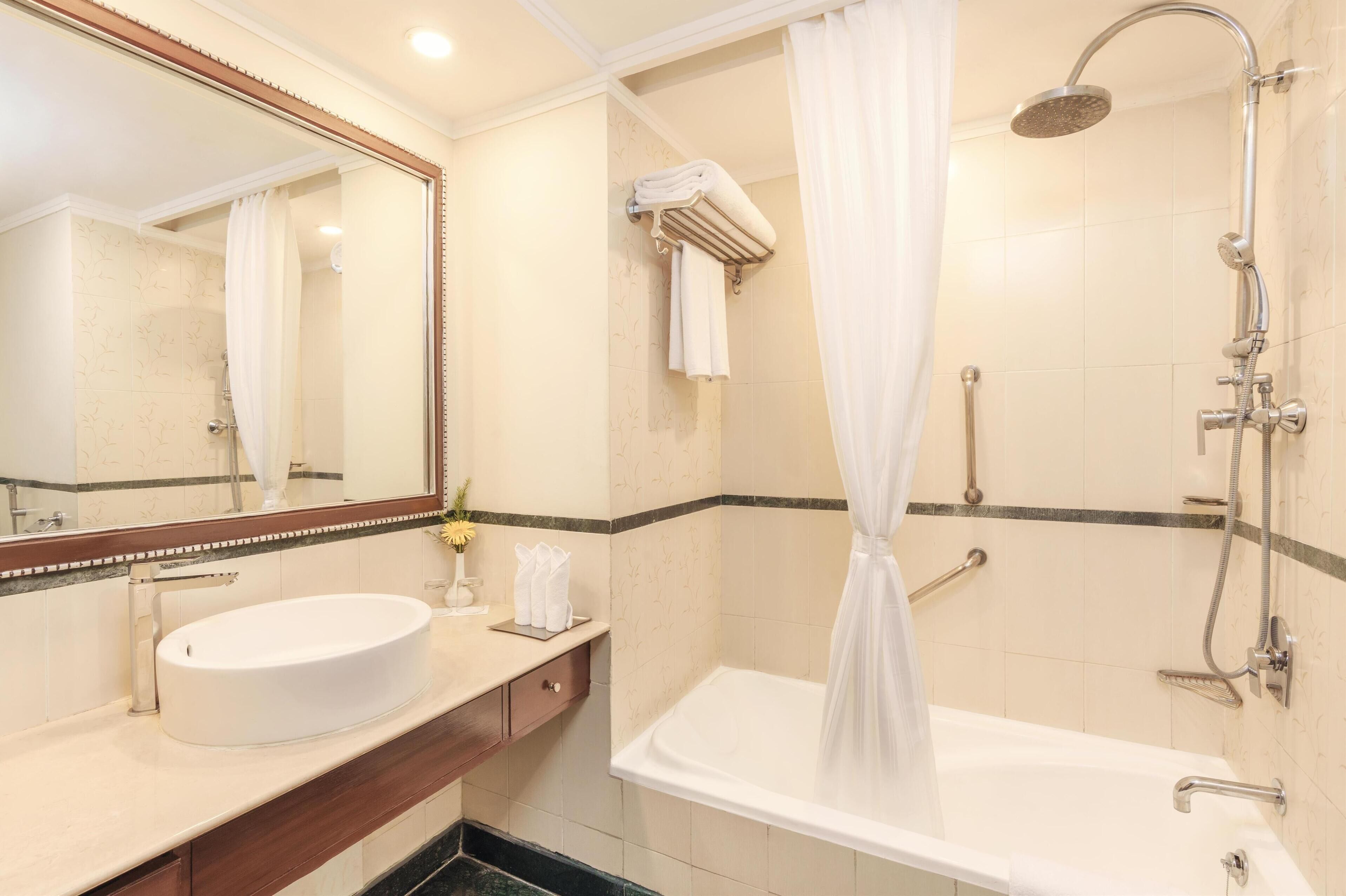 A bathroom with a white sink, a large mirror, a shower with a curtain, and a bathtub.