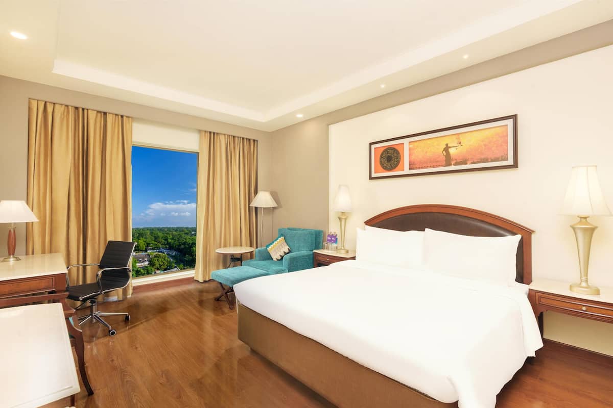 A hotel room with a large bed, a desk, a chair, and a view of the outdoors.