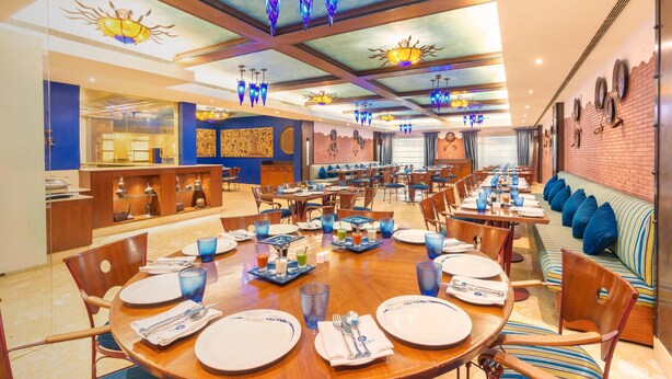 A restaurant with round tables set for dining, blue glassware, and a brick wall with decorative plates. - Radisson Hotel Varanasi (Varanasi)