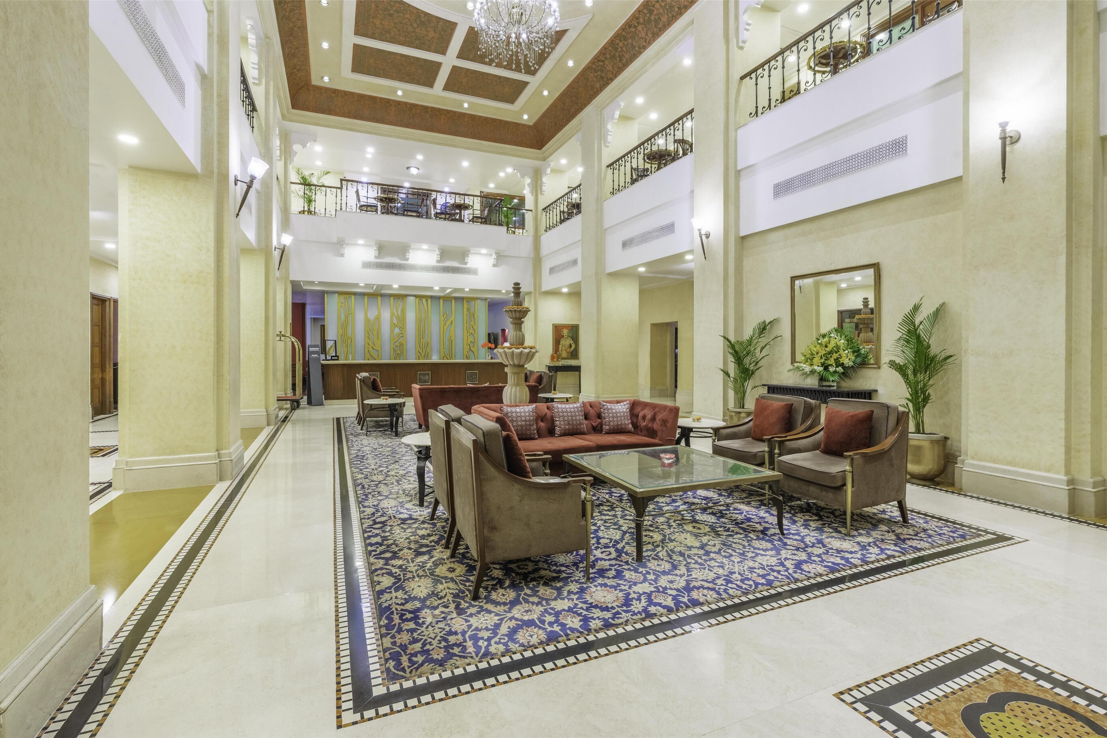 A spacious lobby with a high ceiling, ornate chandeliers, and a central seating area with sofas and armchairs.