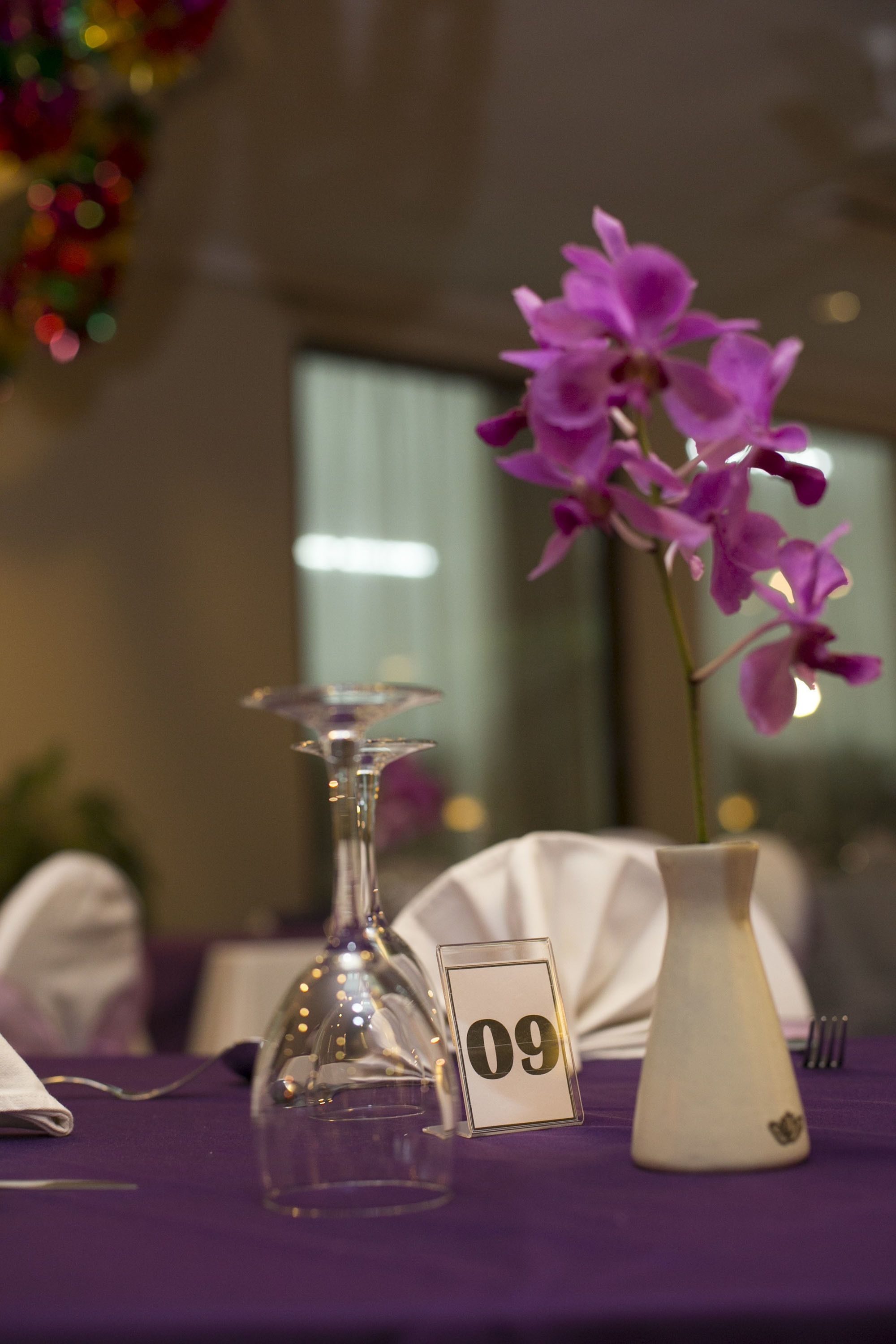 A table with a purple tablecloth, a glass vase with purple flowers, a white vase, and a number sign '09'.