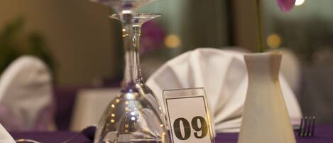 A table with a purple tablecloth, a glass vase with purple flowers, a white vase, and a number sign '09'.