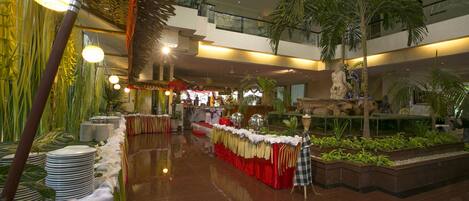 A spacious indoor area with a polished floor, a long buffet table with a red and white tablecloth, and several potted plants.