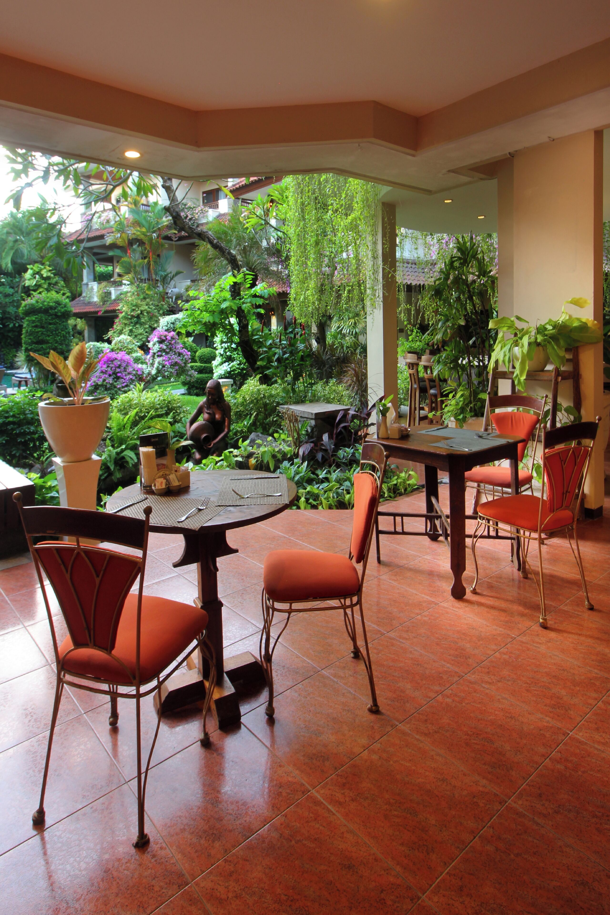 Un comedor con una mesa redonda y cuatro sillas, rodeado de abundante follaje y plantas en macetas.