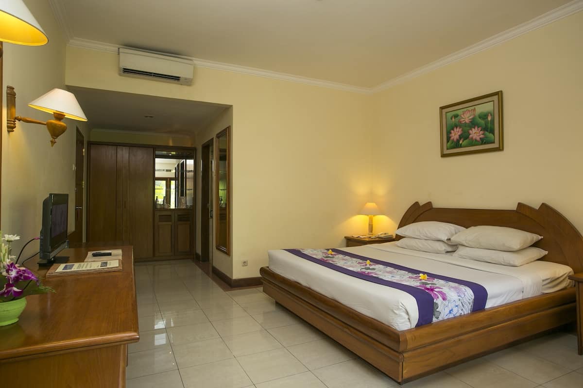 A hotel room with a wooden bed, bedside lamps, a desk with a lamp, a mirror, and a framed picture on the wall.