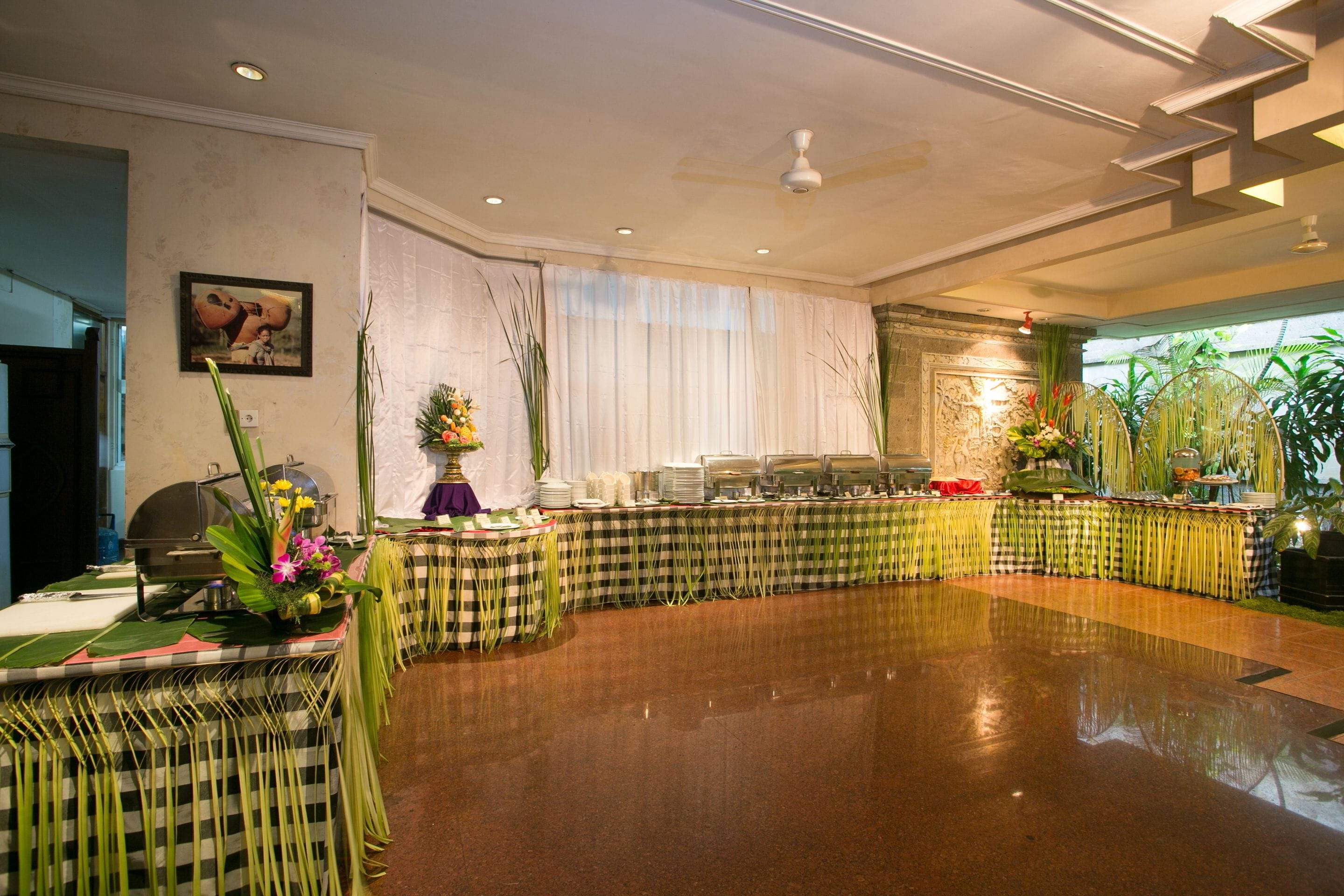 A spacious banquet hall with a polished floor, a buffet setup, and decorative plants.