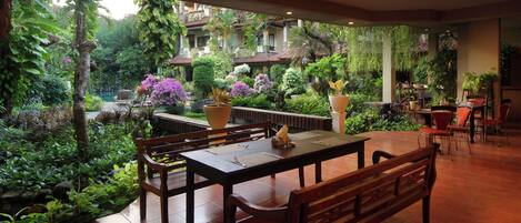 Un jardín interior con zona de comedor que incluye una mesa y bancos, rodeado de abundante follaje y plantas en macetas.