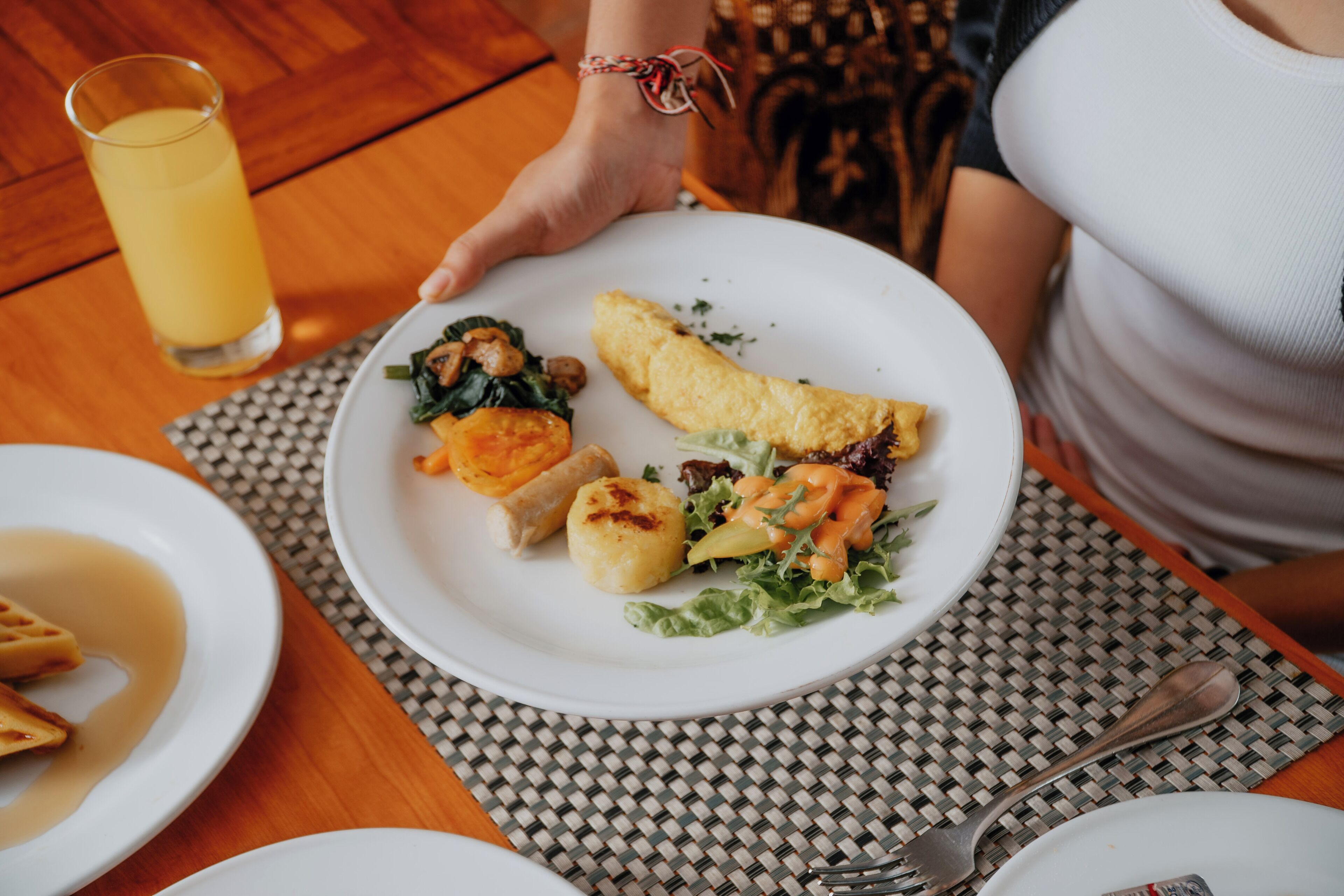 A dining table with a plate of food, a glass of orange juice, and a fork and spoon.