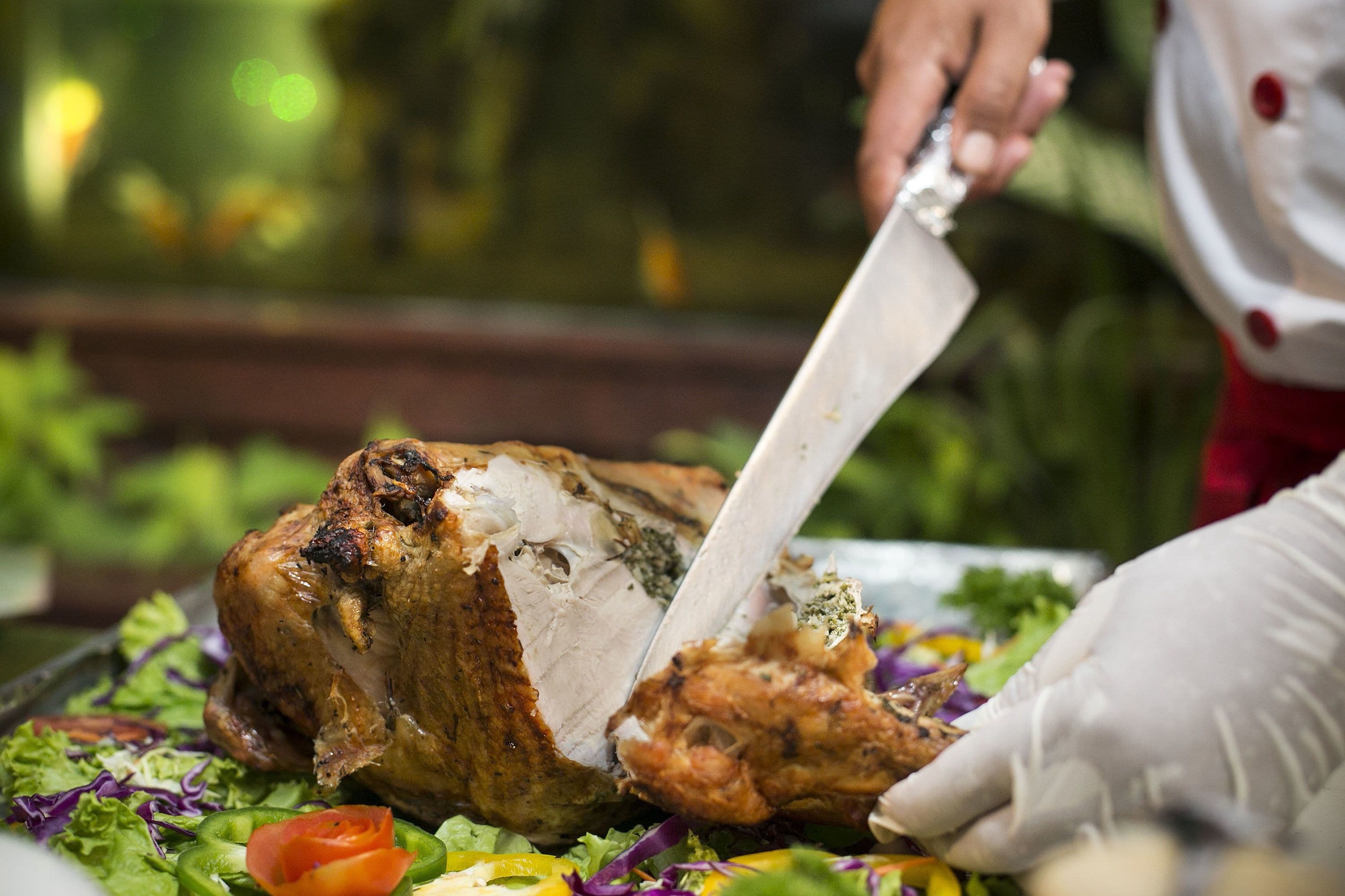 A person slicing a roasted chicken on a platter with vegetables.