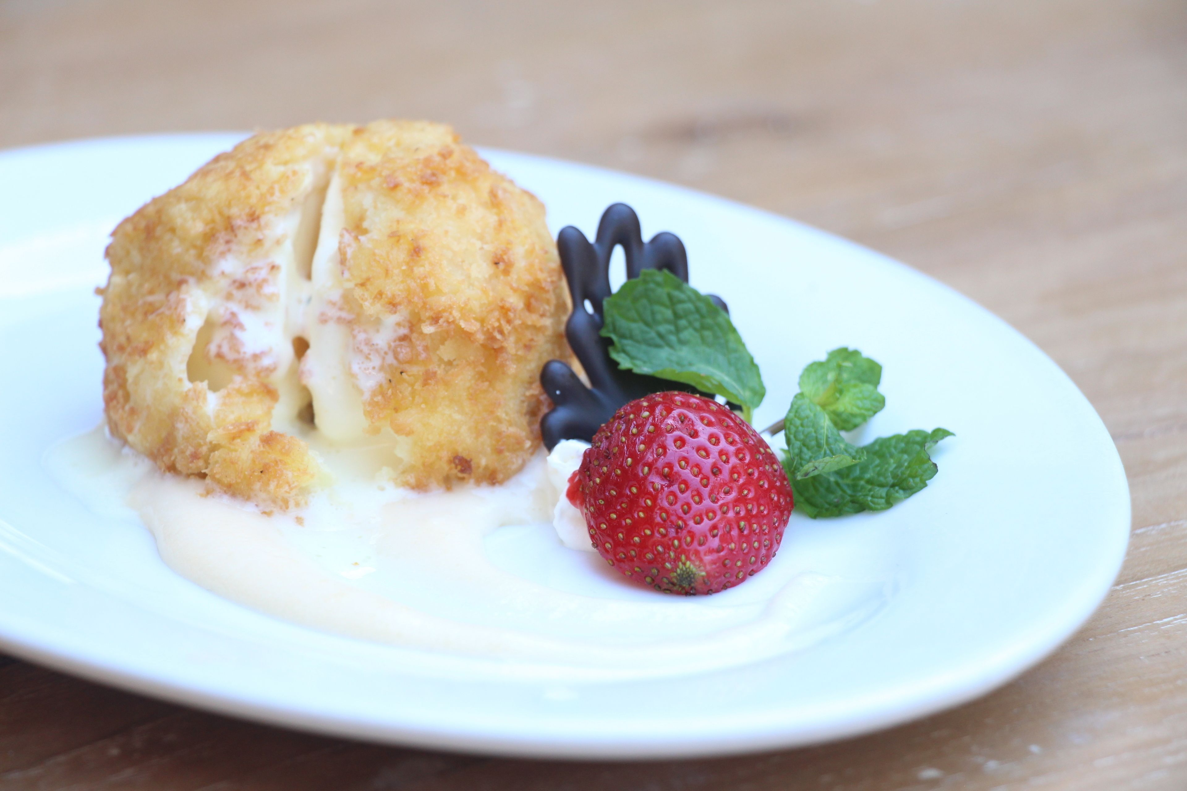 A dessert plate with a baked item, a strawberry, and a mint leaf.