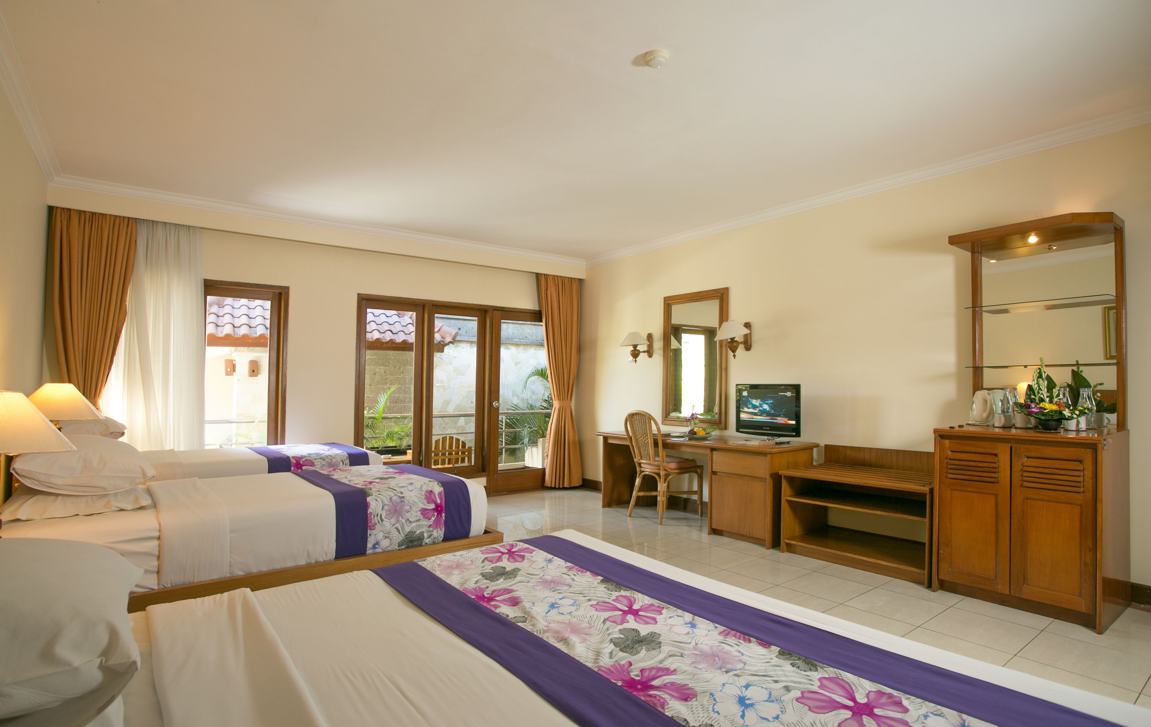 A hotel room with two beds, a desk with a TV, a chair, a wooden cabinet, and a balcony with curtains.