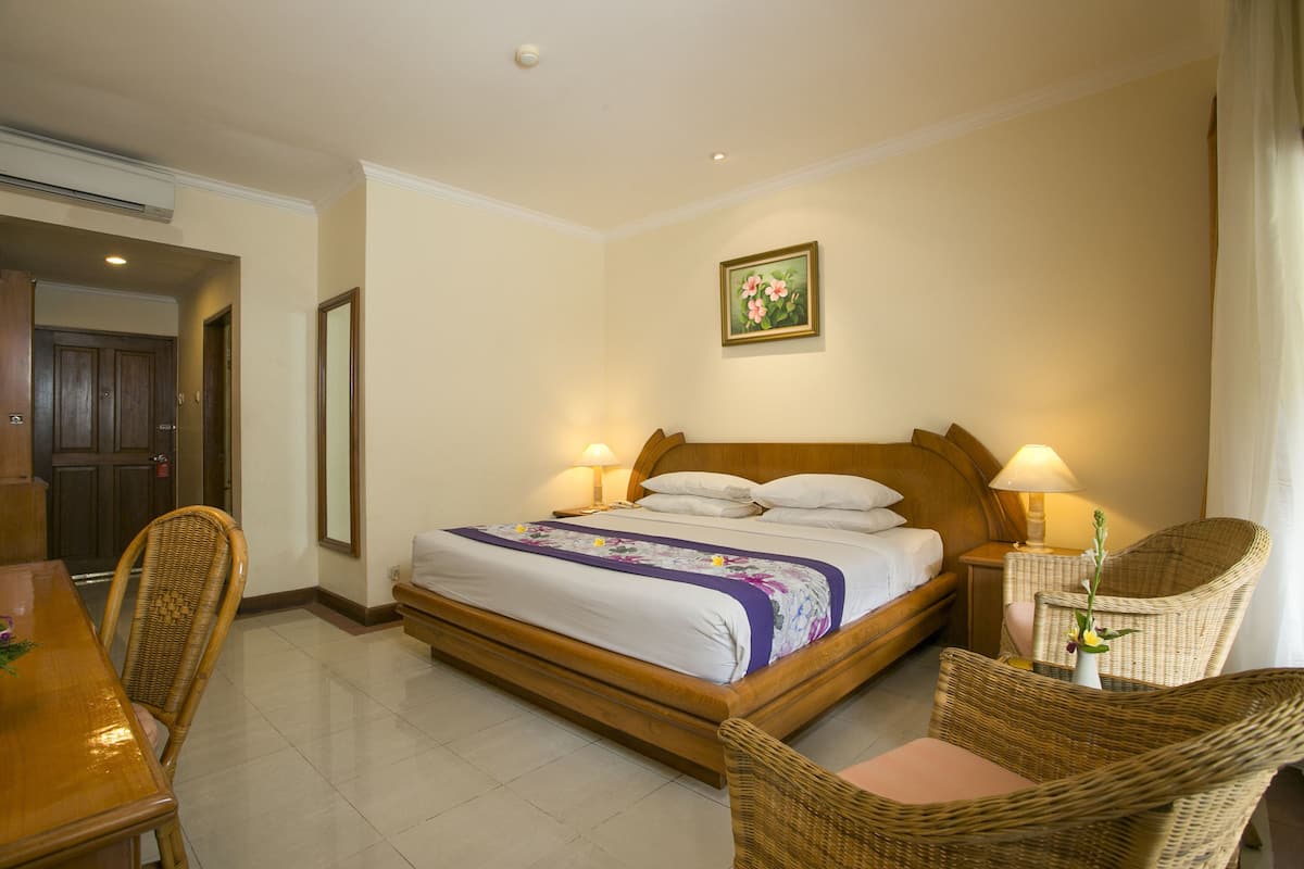 A bedroom with a bed, two bedside tables with lamps, a chair, a dining table, and a door.