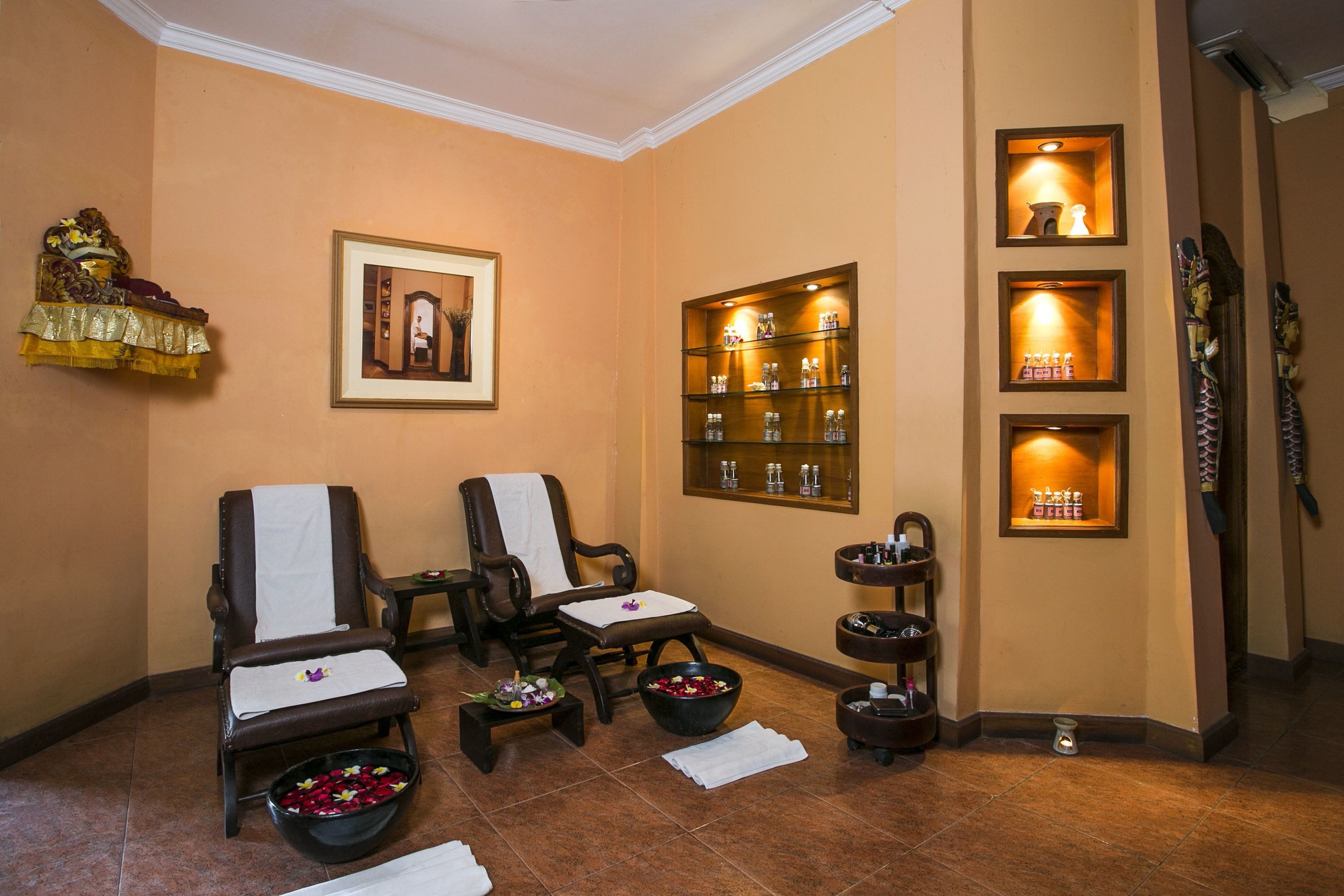 A spa room with two massage chairs, a framed picture, shelves with bottles, and a decorative shelf with flowers.