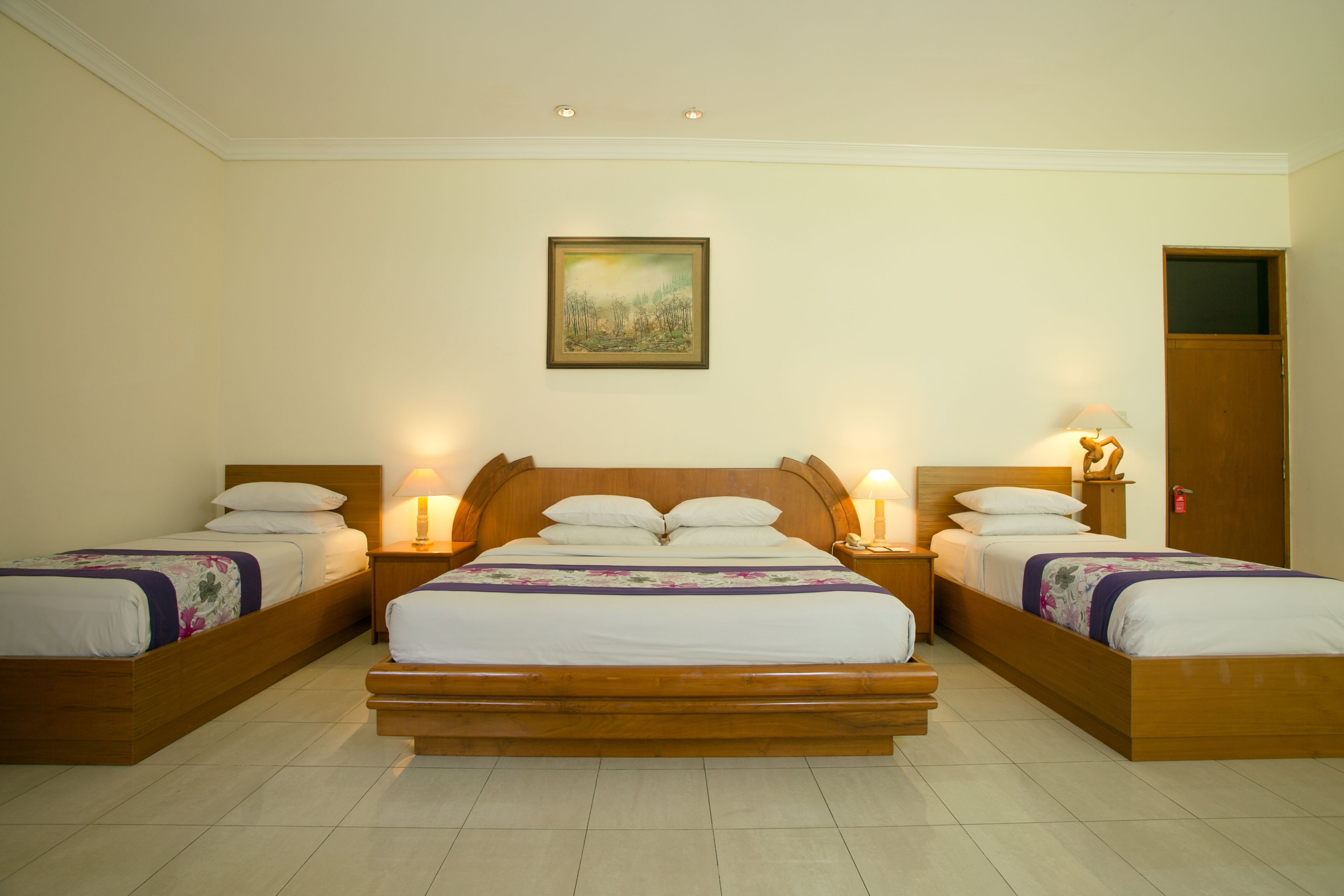 A hotel room with a large bed, two bedside tables with lamps, a wooden headboard, and a painting on the wall.