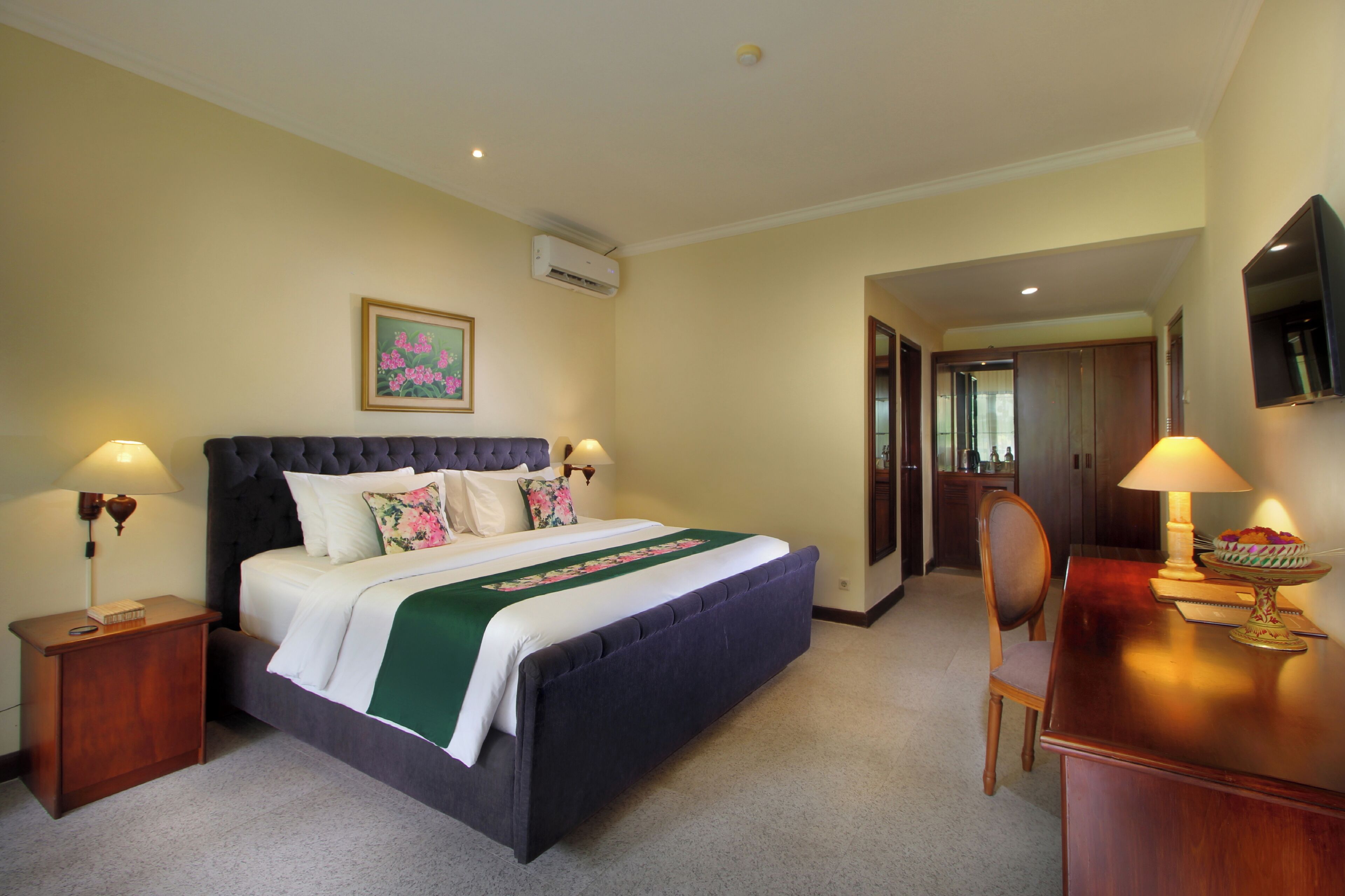 A hotel room with a large bed, bedside lamps, a desk with a lamp, and a television on the wall.