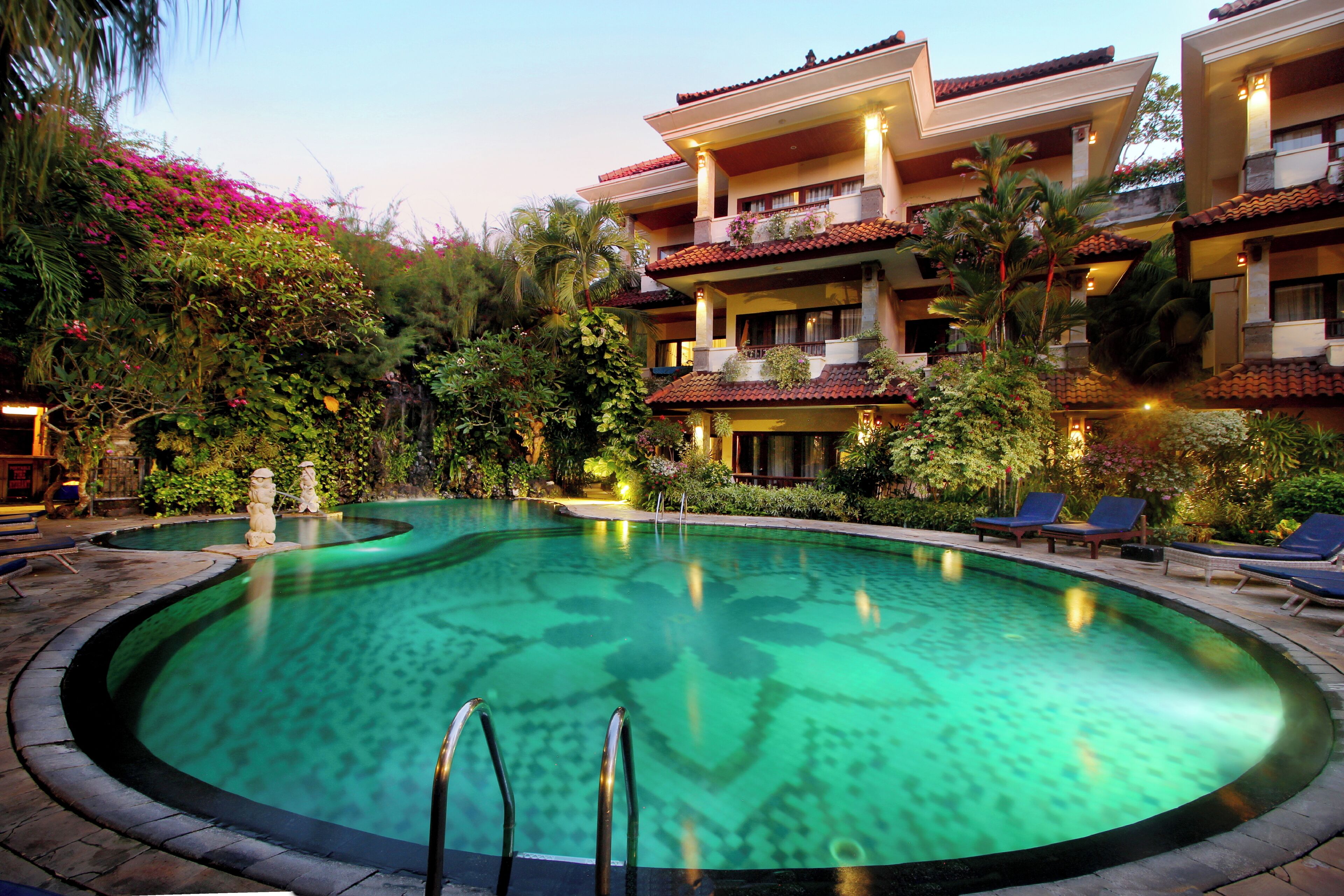 A hotel with a swimming pool, multiple balconies, and lush greenery.