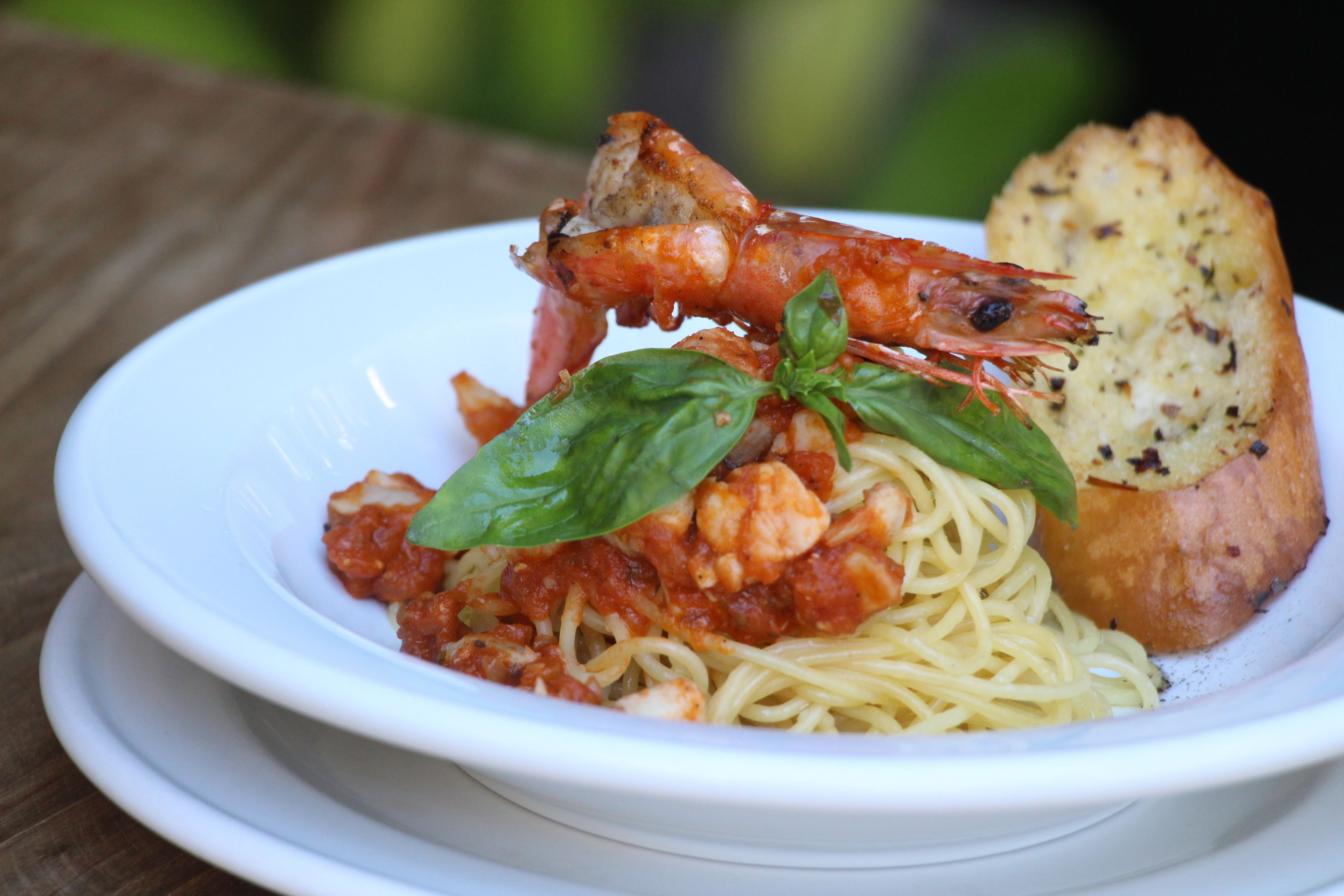 A plate of spaghetti with shrimp and basil, accompanied by a slice of bread.
