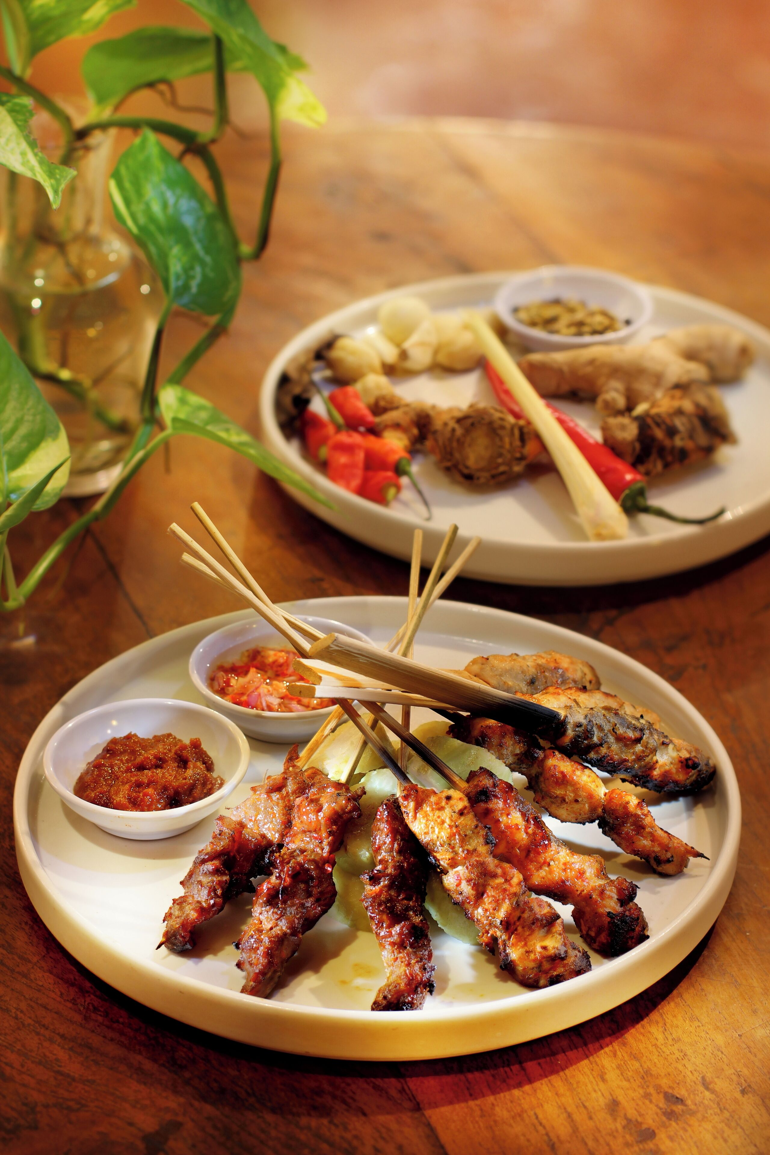 A plate of grilled meat skewers with dipping sauces and a bowl of vegetables.