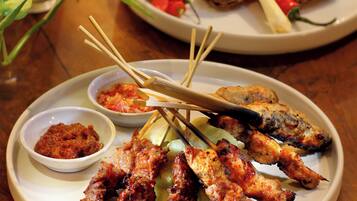 A plate of grilled meat skewers with dipping sauces and a bowl of vegetables.