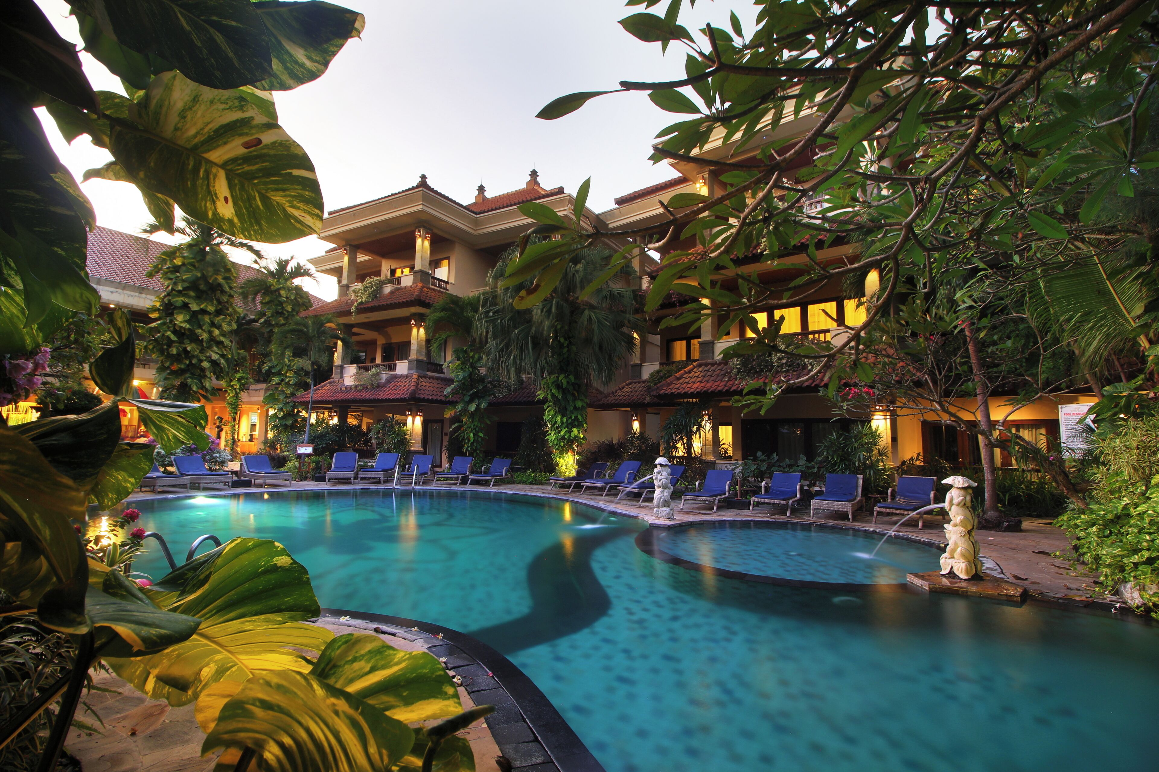 A hotel with a swimming pool surrounded by lounge chairs and tropical plants.