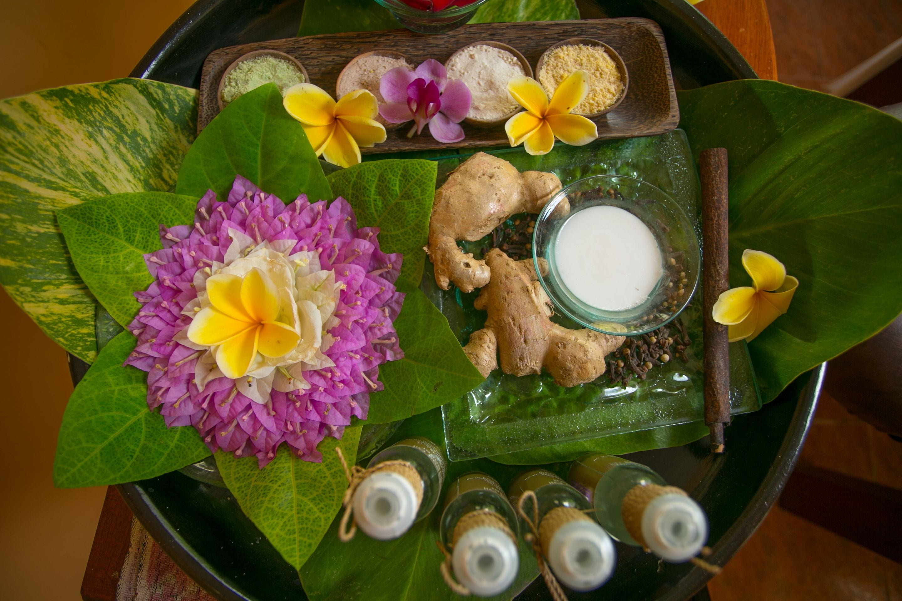 A tray with a glass of milk, ginger slices, and a flower arrangement on a green leaf.