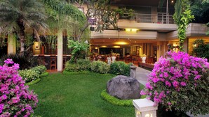 A hotel lobby with a lush garden, seating areas, and a dining space. - Parigata Resort & Spa (Denpasar)