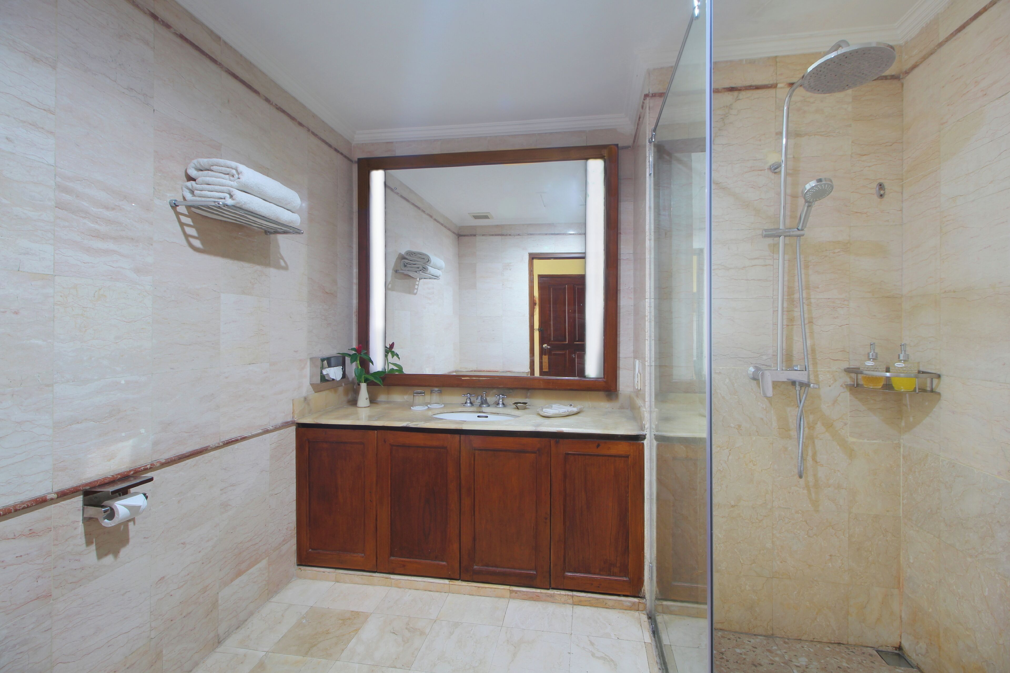 Un baño con pared de mármol, muebles de madera, cabina de ducha de vidrio y espejo sobre el lavabo.