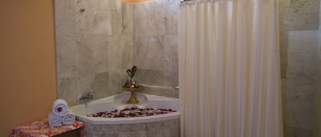A bathroom with a bathtub, shower curtain, and a small table with towels and a flower arrangement.
