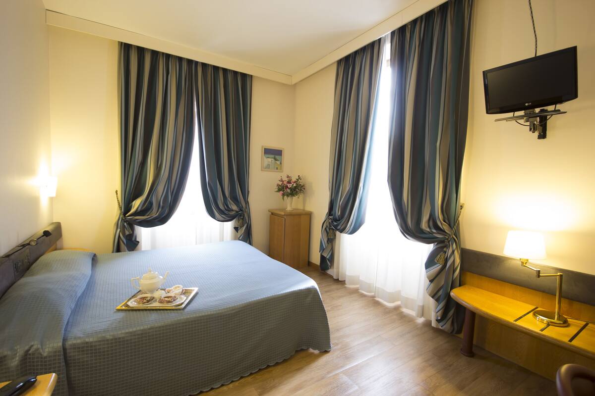 A hotel room with a bed, a desk, a TV, and curtains.