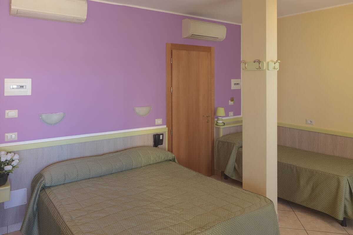 A bedroom with a single bed, a bedside table, a lamp, and a mirror.