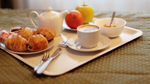 A tray with croissants, a cup of coffee, a teapot, a bowl with a spoon, and a plate with an apple and a lemon. - Hotel Arco Romana (Milan)