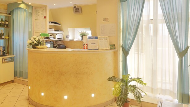 A reception area with a curved counter, a potted plant, and a window with sheer curtains. - Hotel Arco Romana (Milan)
