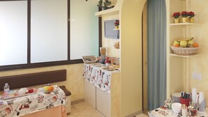 A dining area with a table set for a meal, a television mounted on the wall, and a shelf with fruits and flowers. - Hotel Arco Romana (Milan)