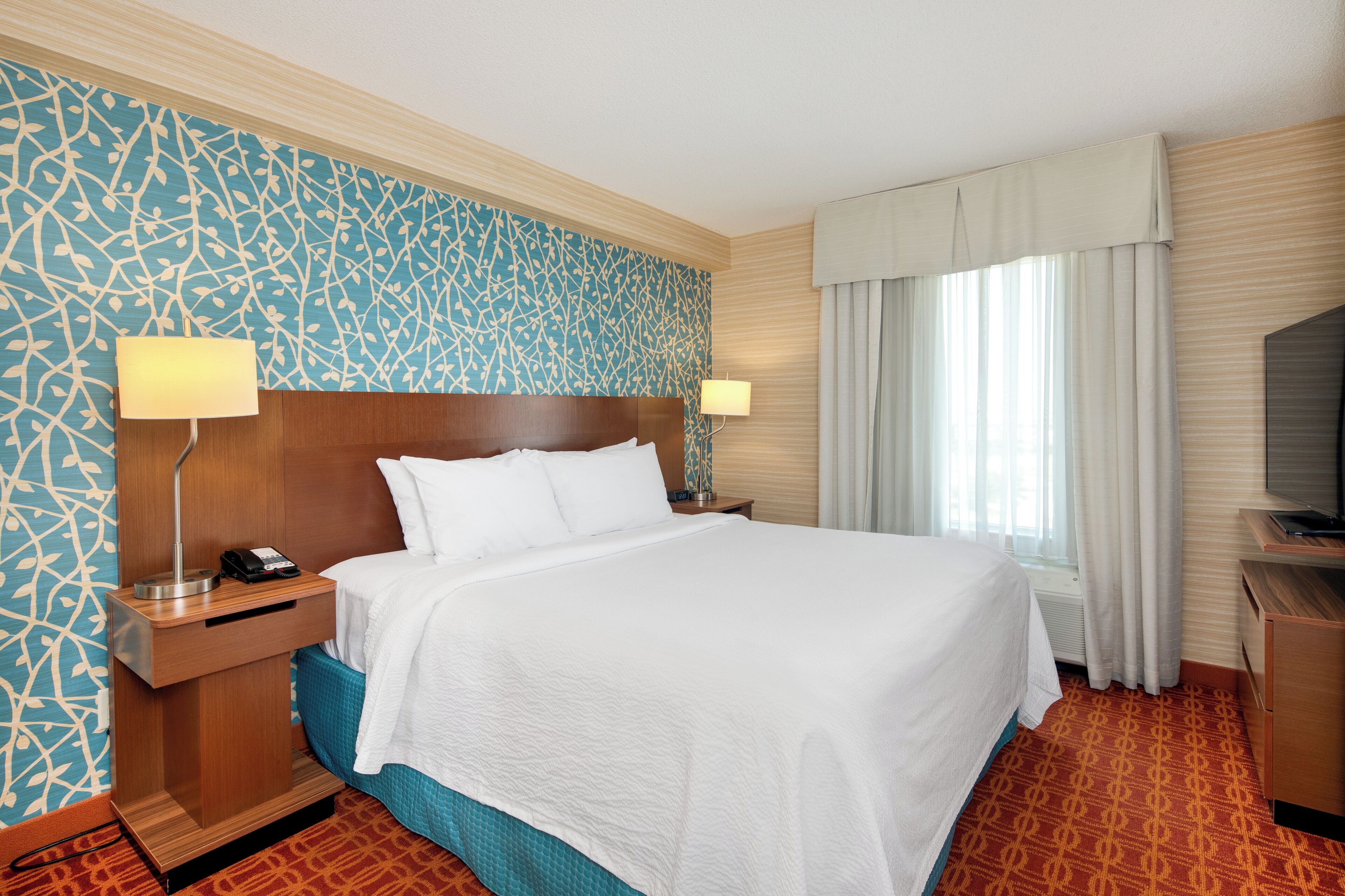 A hotel room with a large bed, two bedside tables with lamps, a TV, and a patterned wall.