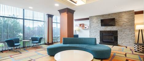 A modern lobby with a large window, a stone fireplace, and seating areas.