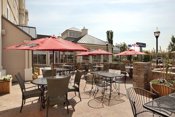 Un espace extérieur aménagé en terrasse, avec des tables et des chaises, des parasols rouges et un mur en briques.