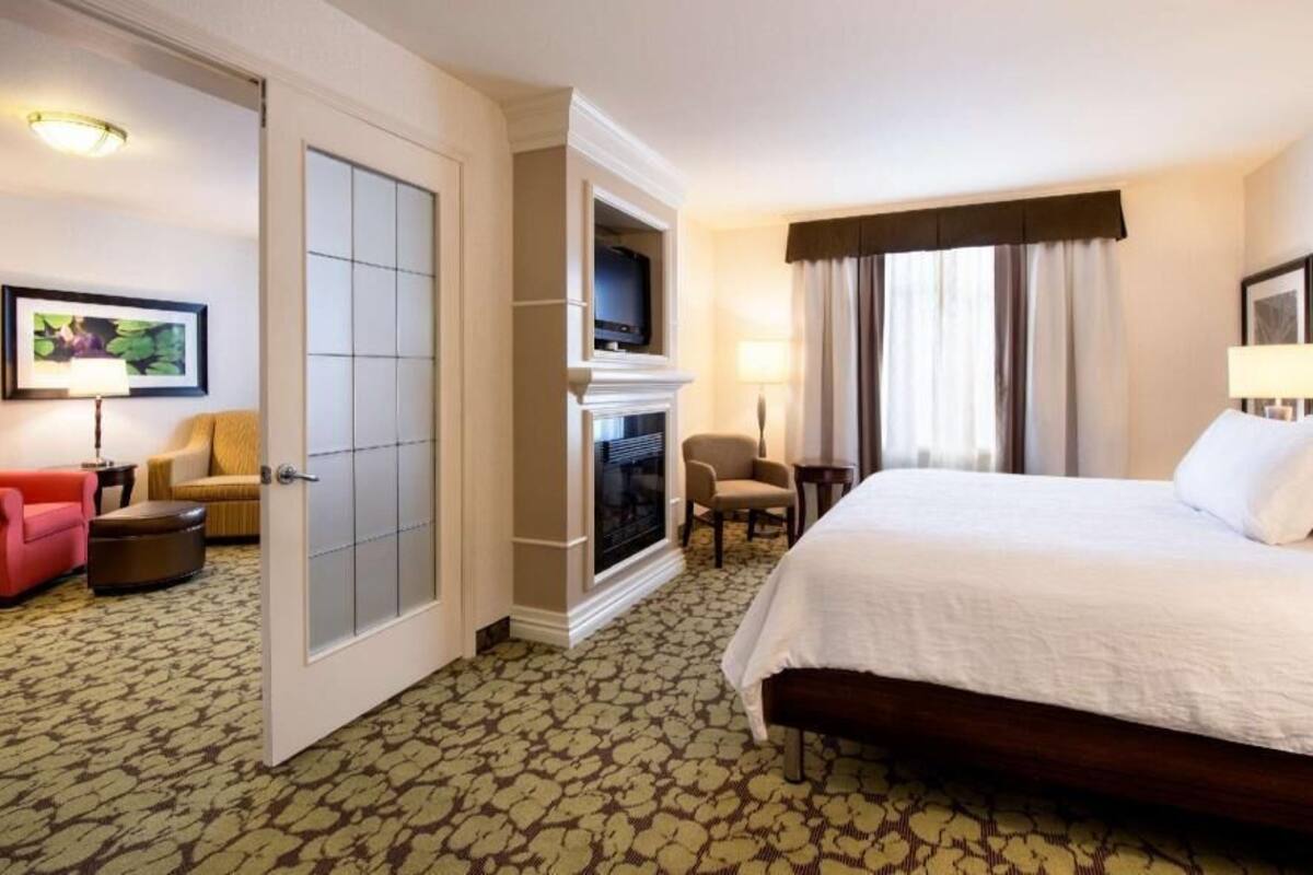 A hotel room with a bed, a fireplace, a television, a desk, and a chair.